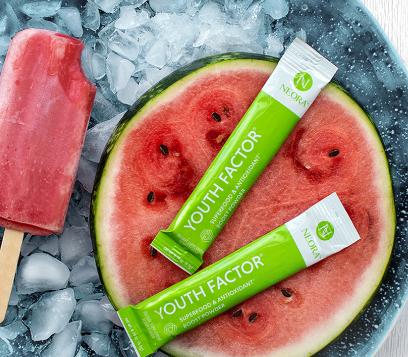 Neora's Youth Factor Antioxidant Powder laying atop a watermelon next to a popsicle